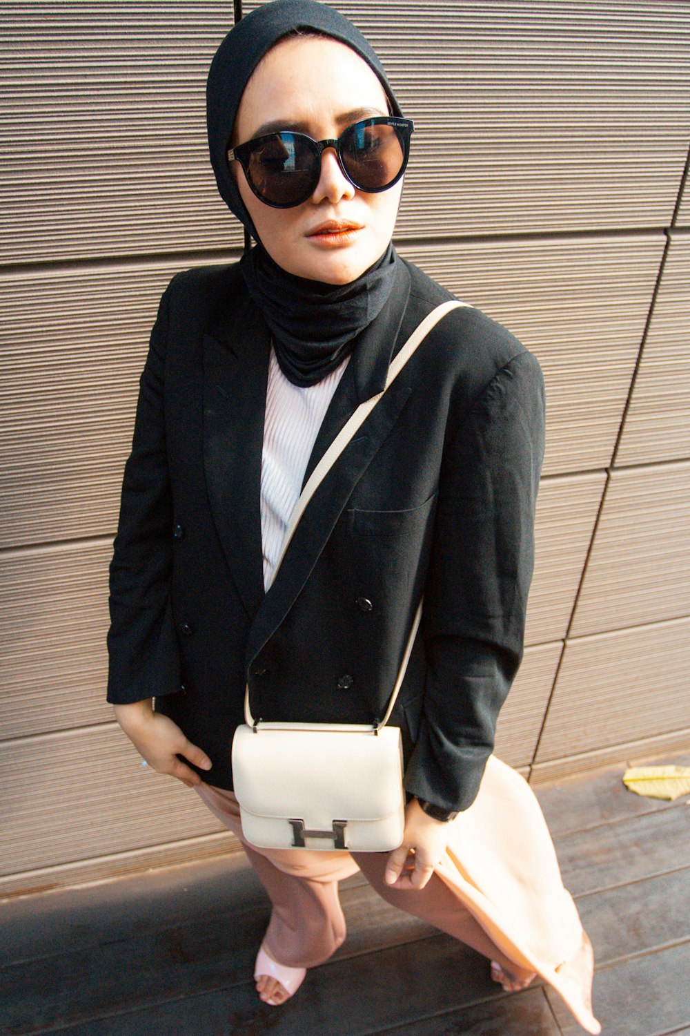 a woman in a black jacket and sunglasses holding a white purse