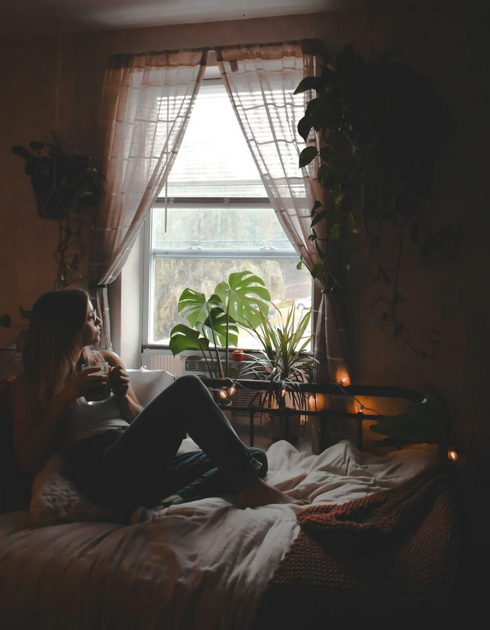 une femme assise sur un lit devant une fenêtre
