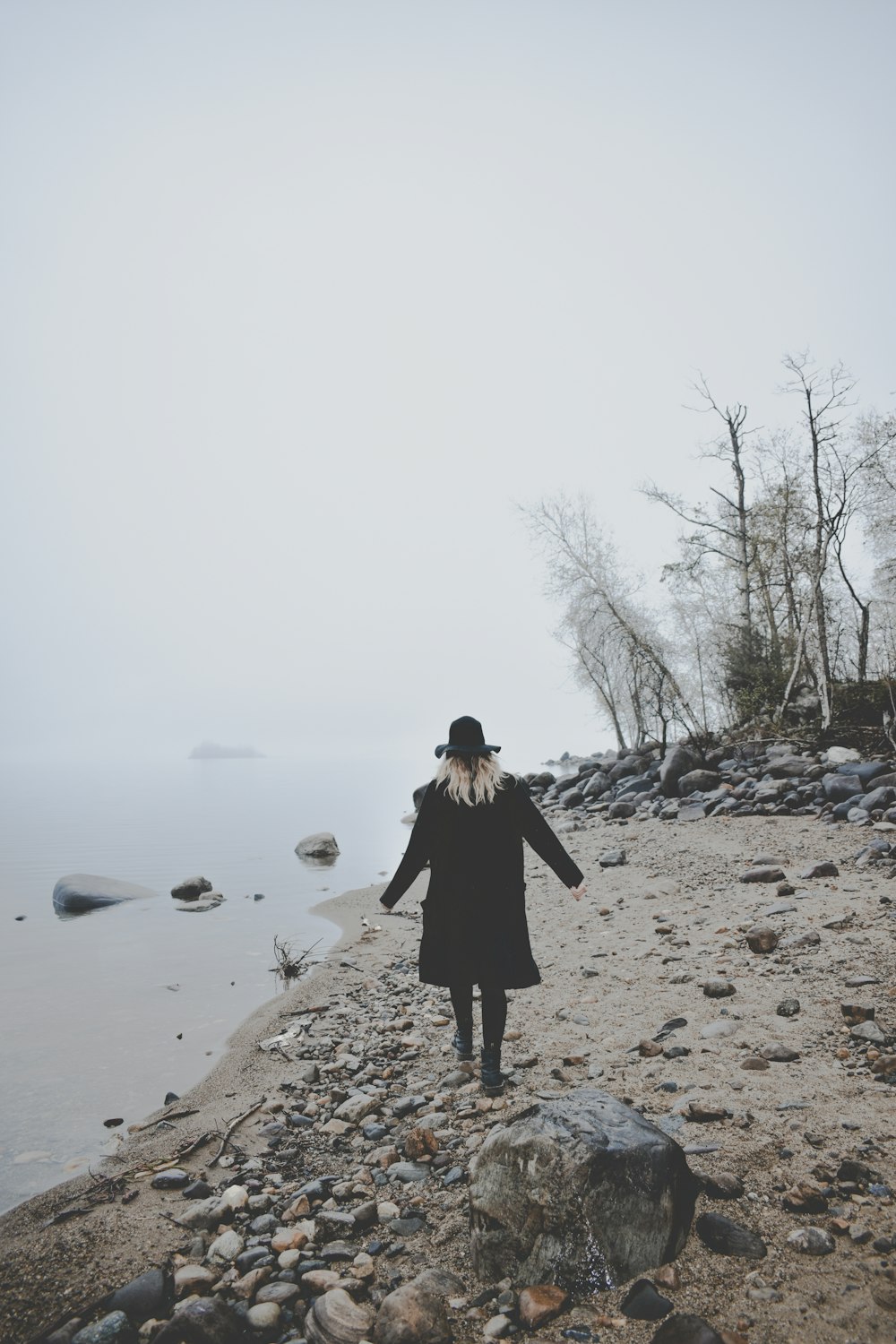 a woman standing on a rocky beach next to the ocean