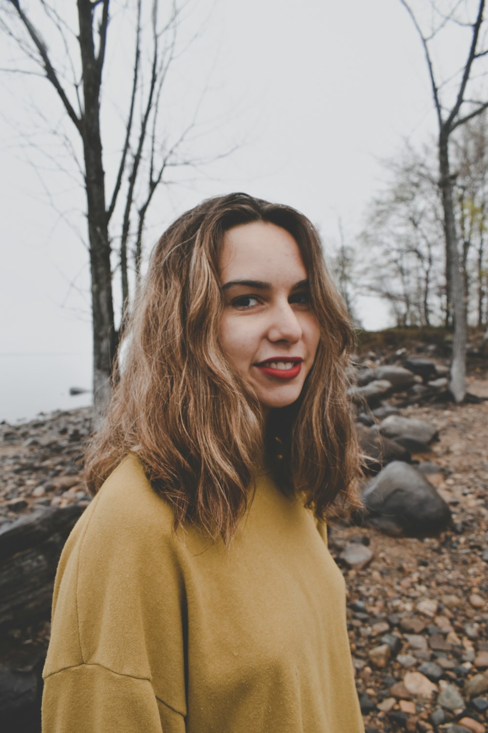 a woman standing on a rocky beach with trees in the background