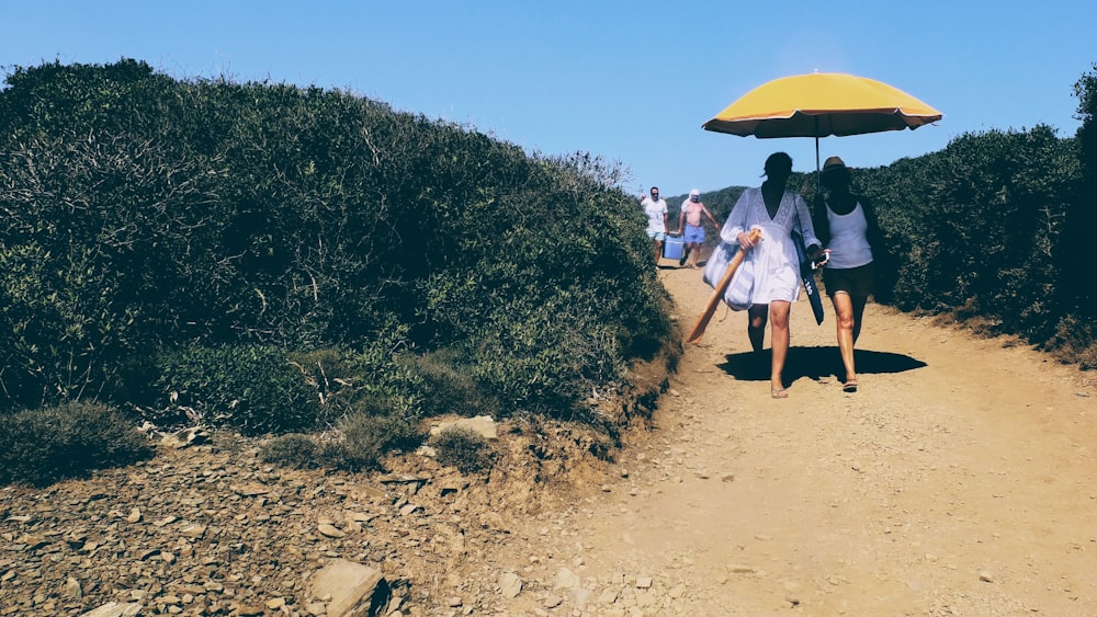 a group of people walking down a dirt road under an umbrella