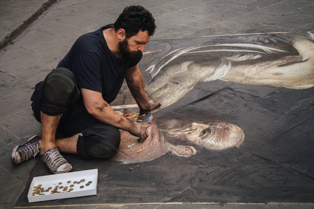 a man sitting on the ground working on a painting