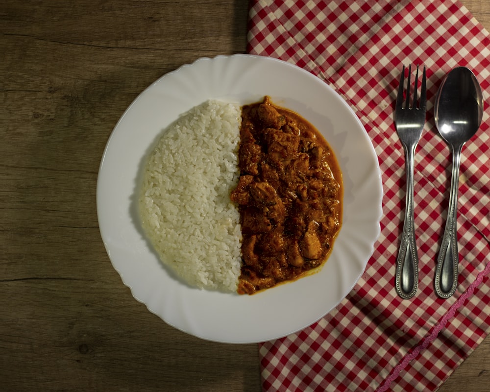 um prato branco coberto com arroz e carne ao lado de um garfo