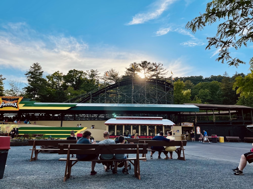 a group of people sitting at picnic tables in front of a roller coaster