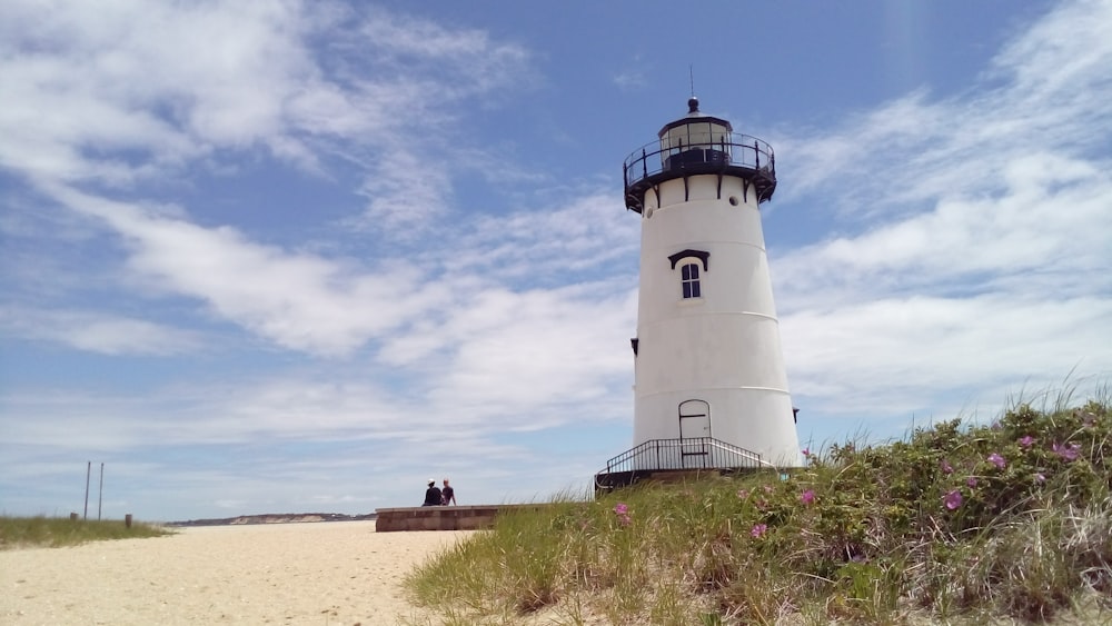 a couple sitting on a bench next to a lighthouse