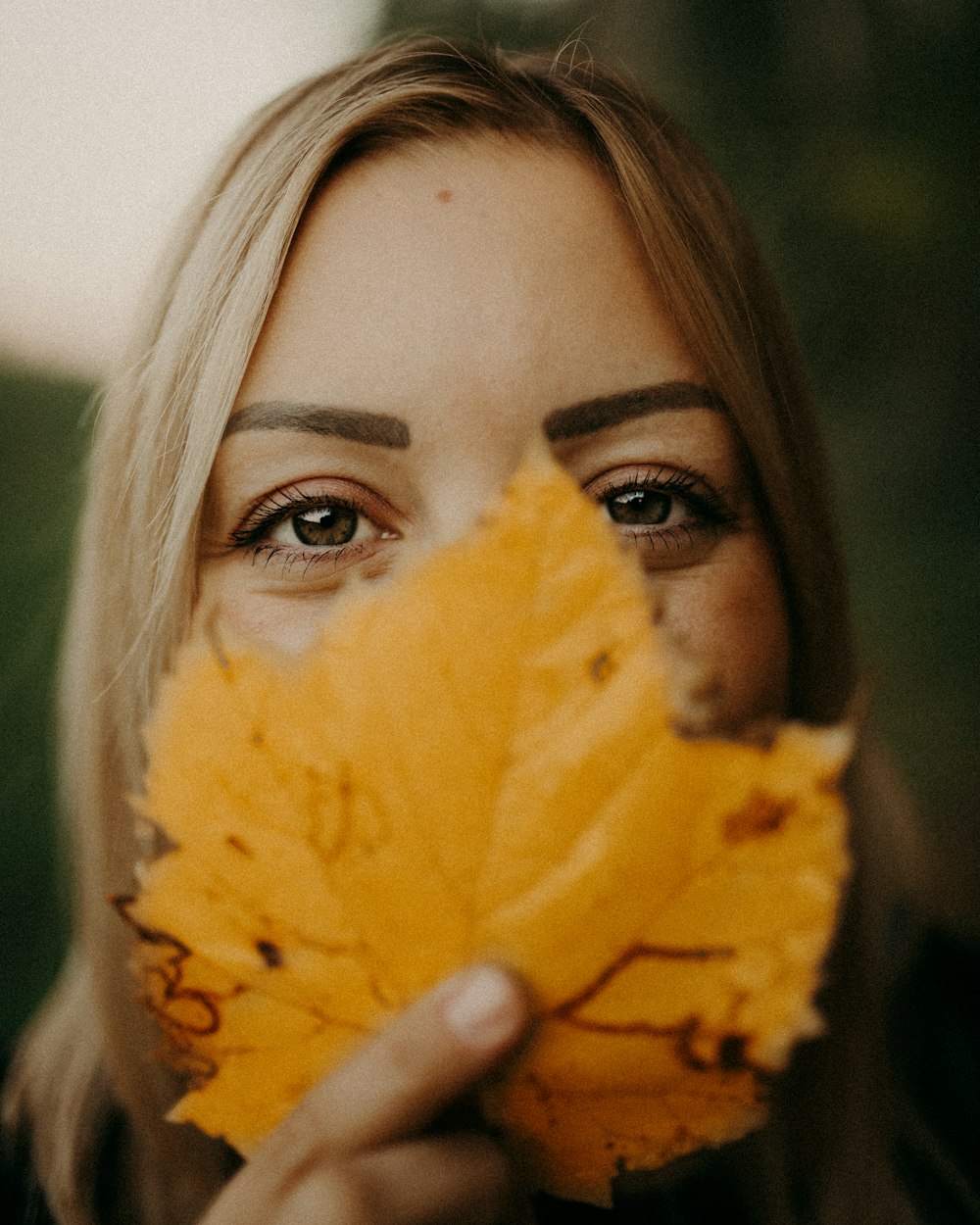a woman holding a yellow leaf in front of her face