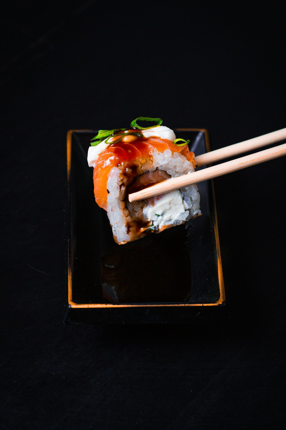 um prato preto coberto com sushi e pauzinhos