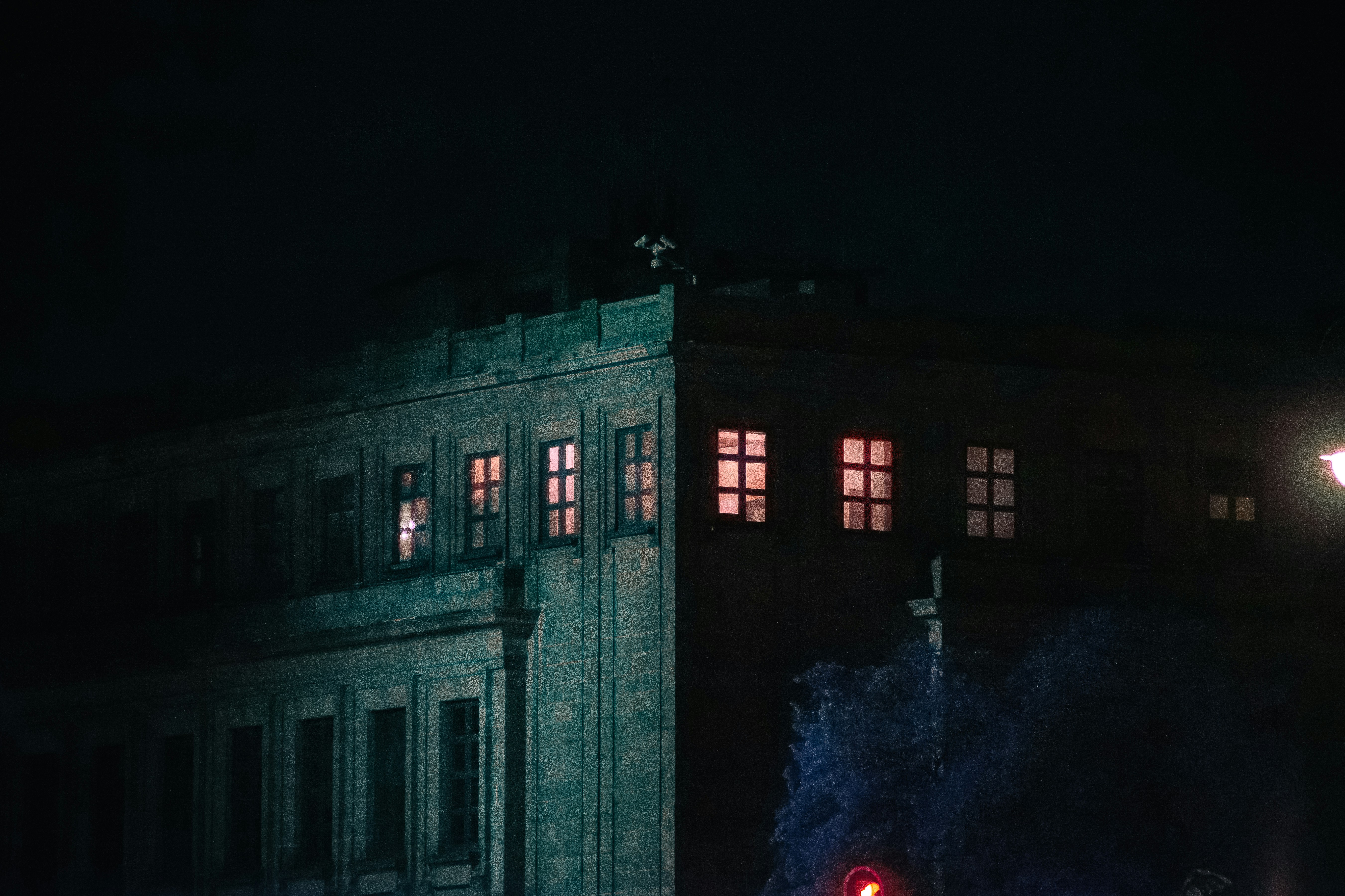 High-rise commercial building exterior at night, multiple security cameras visible, city lights below, dark dramatic sky