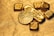 A collection of gold bullion including bars and coins, featuring intricate designs and inscriptions visible on the surfaces. The items are placed on a textured golden background, emphasizing their shiny and luxurious appearance.