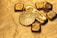 A collection of gold bullion including bars and coins, featuring intricate designs and inscriptions visible on the surfaces. The items are placed on a textured golden background, emphasizing their shiny and luxurious appearance.