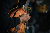 Close-up of a guitarist’s hands mid-strum with a gleaming signed guitar.