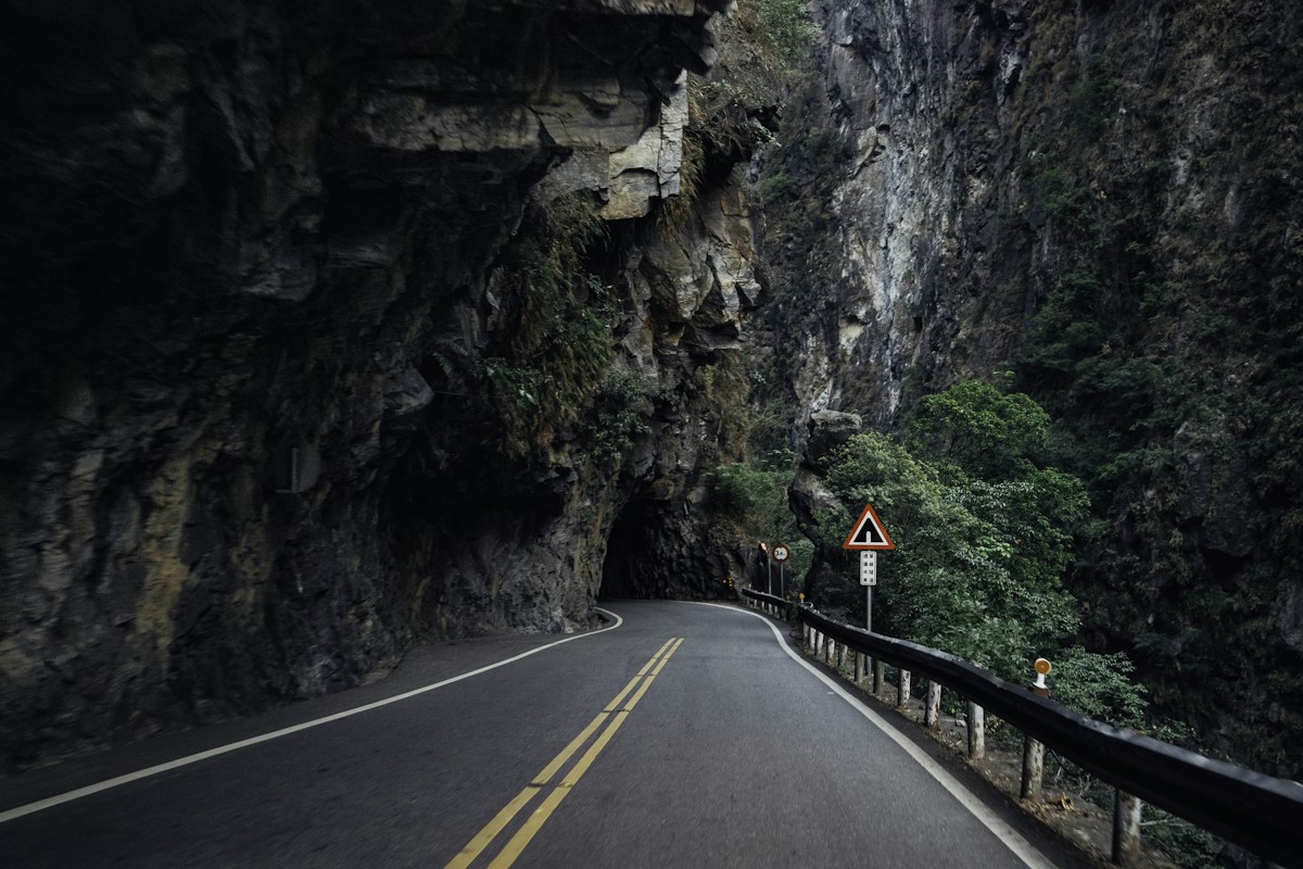 A two-lane road carved beneath a marble cliff