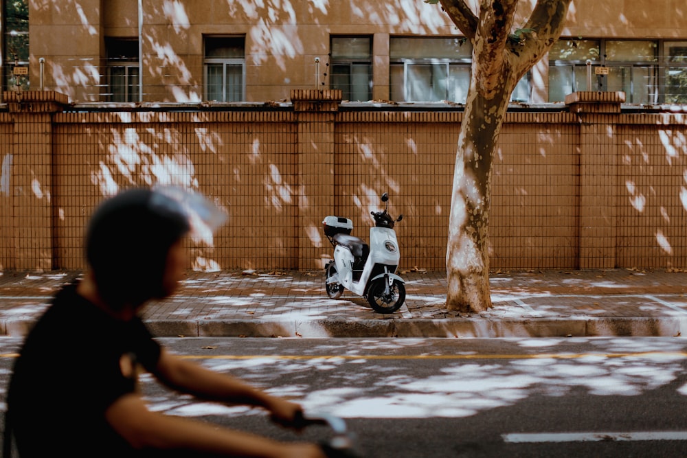 a man riding a scooter down a street next to a tree