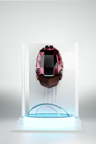 An abstract geometric object, resembling a futuristic helmet, is displayed in the center. The object is made of various metallic and reflective components, primarily black and dark red hues, and is set against a minimalistic backdrop. The object is encased in a transparent glass case with soft ambient lighting illuminating it.