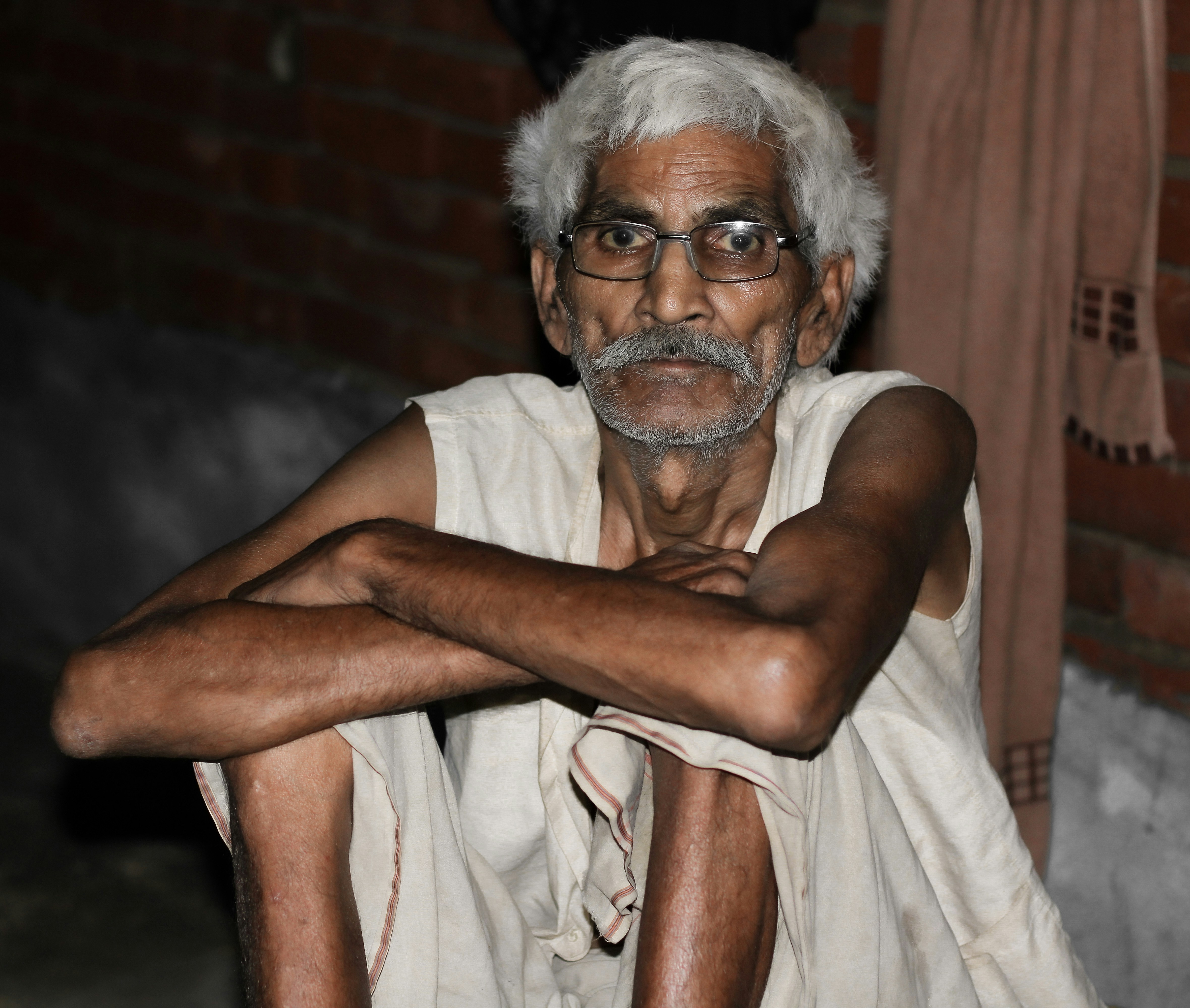 Ein Mann mit weißen Haaren und Brille sitzt vor einer Ziegelmauer