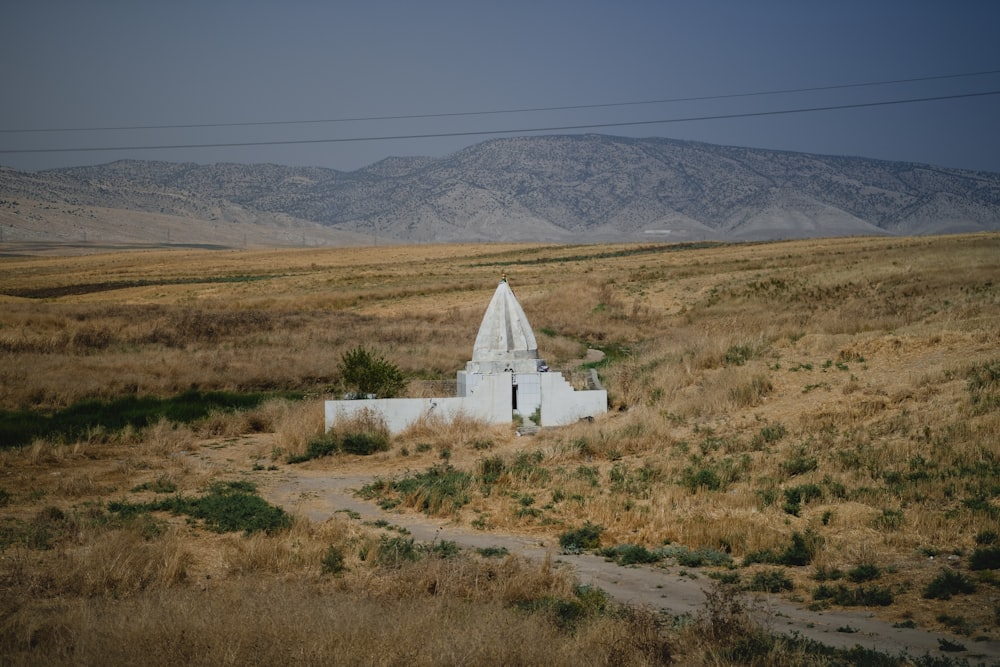 Un pequeño edificio blanco en un campo con montañas al fondo