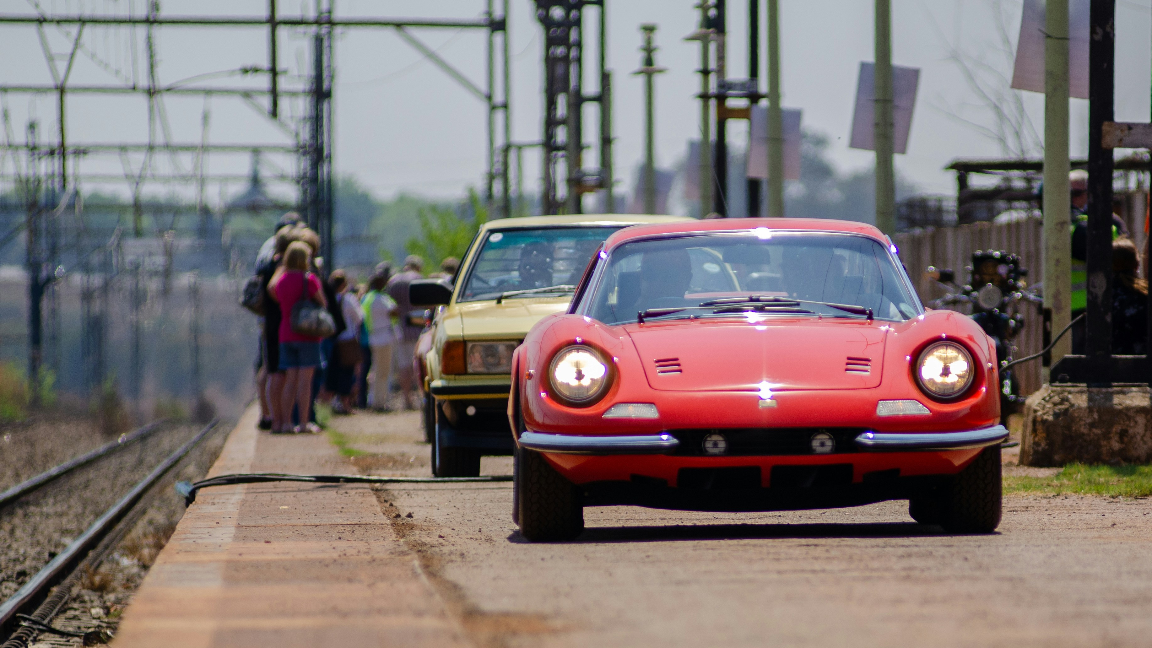 A red car driving down a road next to a train track photo – Free Car ...