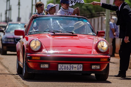 A group of friends smiling and enjoying a drive in a red convertible on a sunny day.