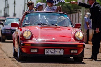 A group of friends smiling and enjoying a drive in a red convertible on a sunny day.