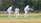 A group of young cricket players wearing matching safety gear, smiling on the pitch.
