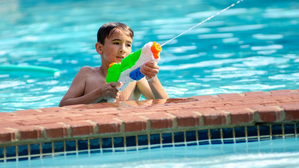 a young boy playing with a water gun in a swimming pool