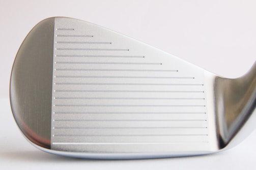 Close-up view of a metallic golf club head with visible grooves and a smooth silver surface, showing intricate craftsmanship and detailing.