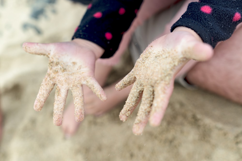 a person holding sand in their hands on the beach
