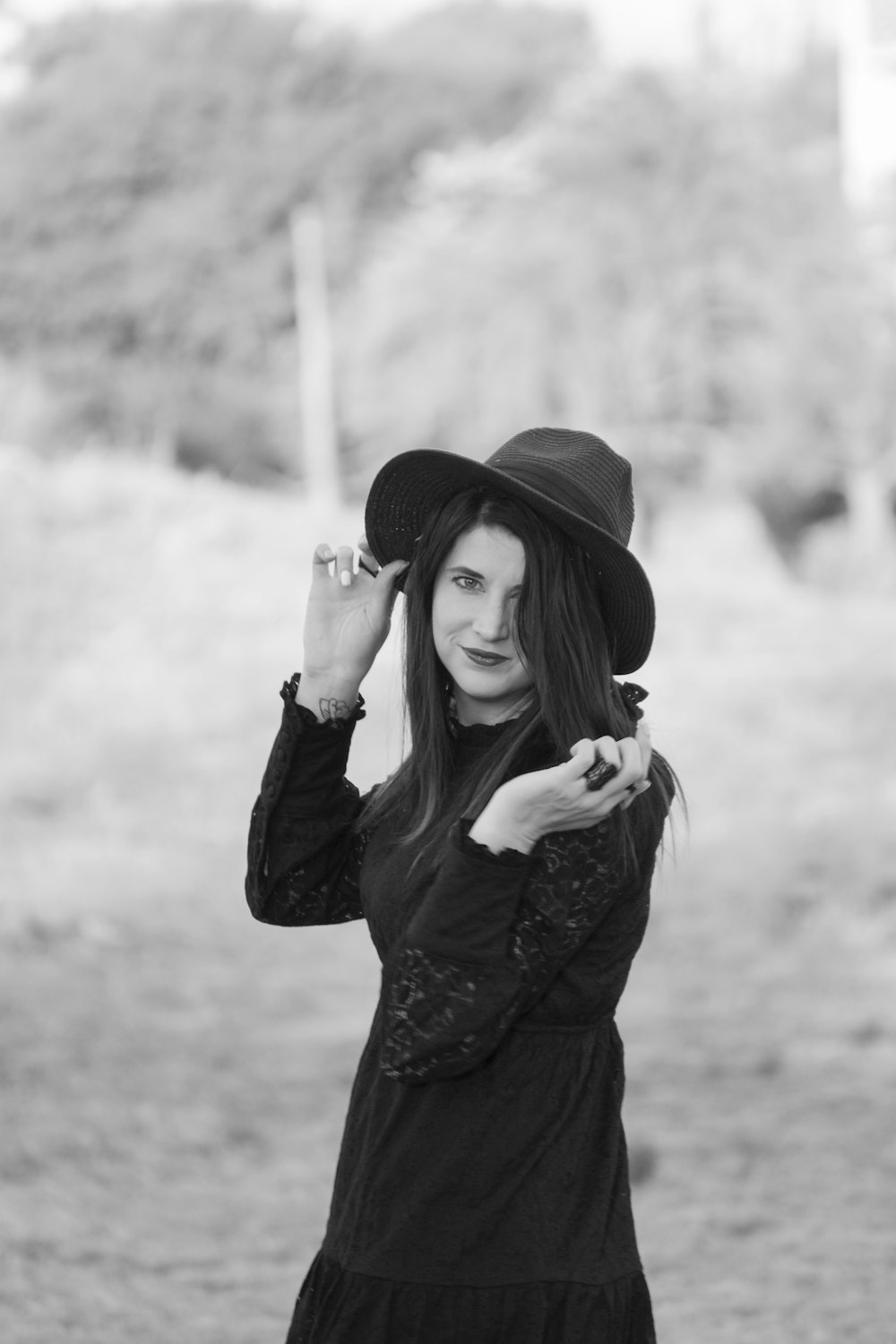 a woman in a black dress and hat poses for a picture