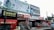 A busy storefront area features multiple signs and advertisements. At the forefront, a large red tractor with the label 'Swaraj 855 FE' is parked. Above the shops, there are prominent billboards for orthopedic capsules and an IVF center. The storefronts include 'Lovely Collection' and 'Shiva Shop' with various products displayed. Coca-Cola branding is visible on signs and awnings. A small motorcycle is parked in front of the shops.