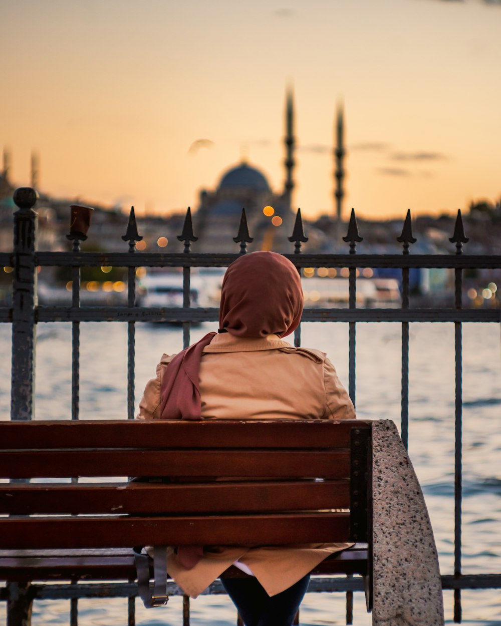 a woman sitting on a bench looking at the water