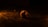 A single twenty-sided die sits on a textured surface, illuminated by warm, low lighting that casts dramatic shadows. The background is mostly dark, emphasizing the die's intricate numbers and facets.