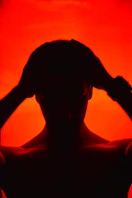 Silhouette of a person holding their head against red background