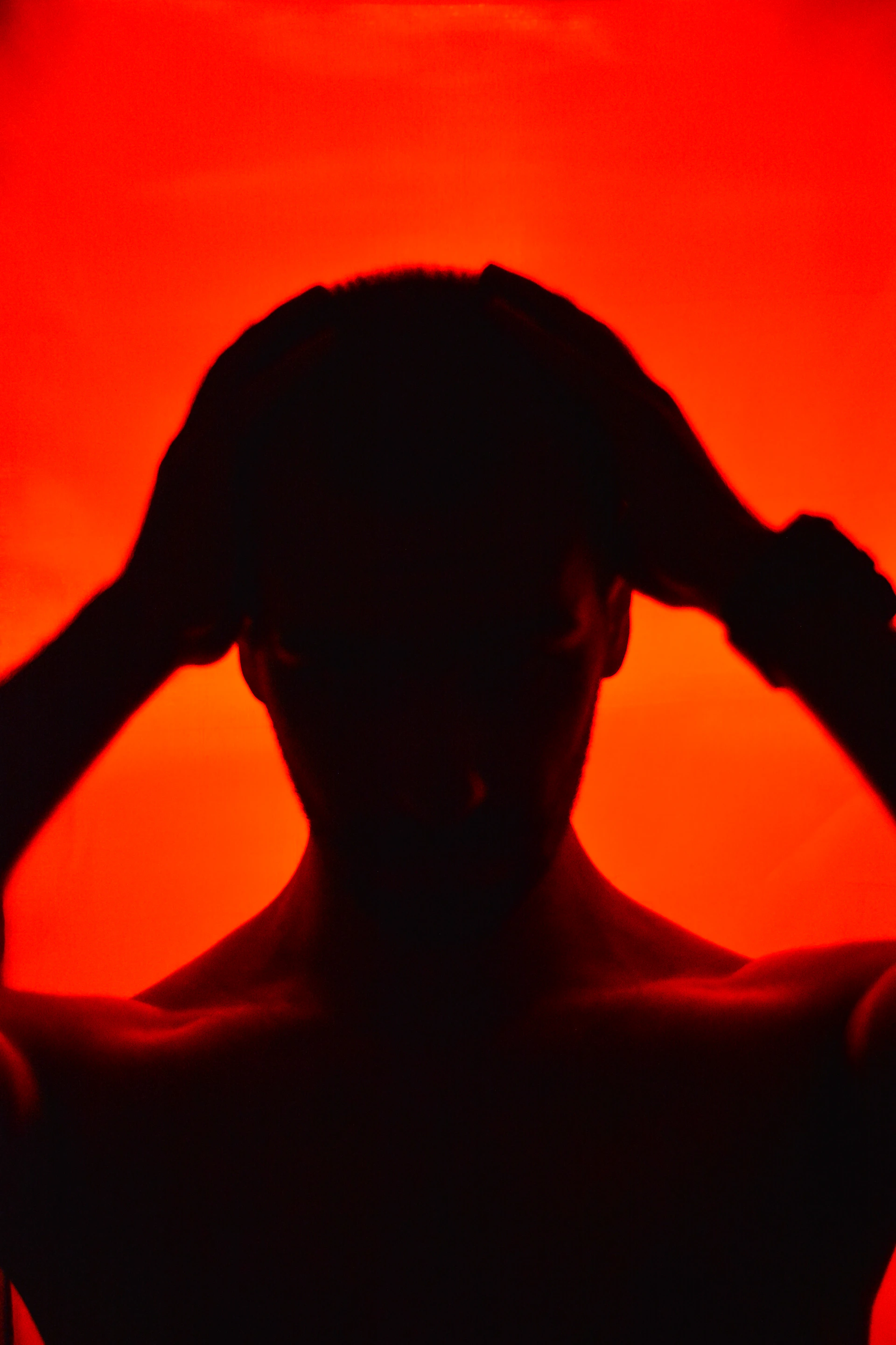 Silhouette of a person holding their head against red background
