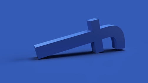A symmetrical, three-dimensional blue structure resembling a manipulated or stylized lowercase 'f' is positioned at an angle on a solid blue surface, creating a modern and abstract visual.