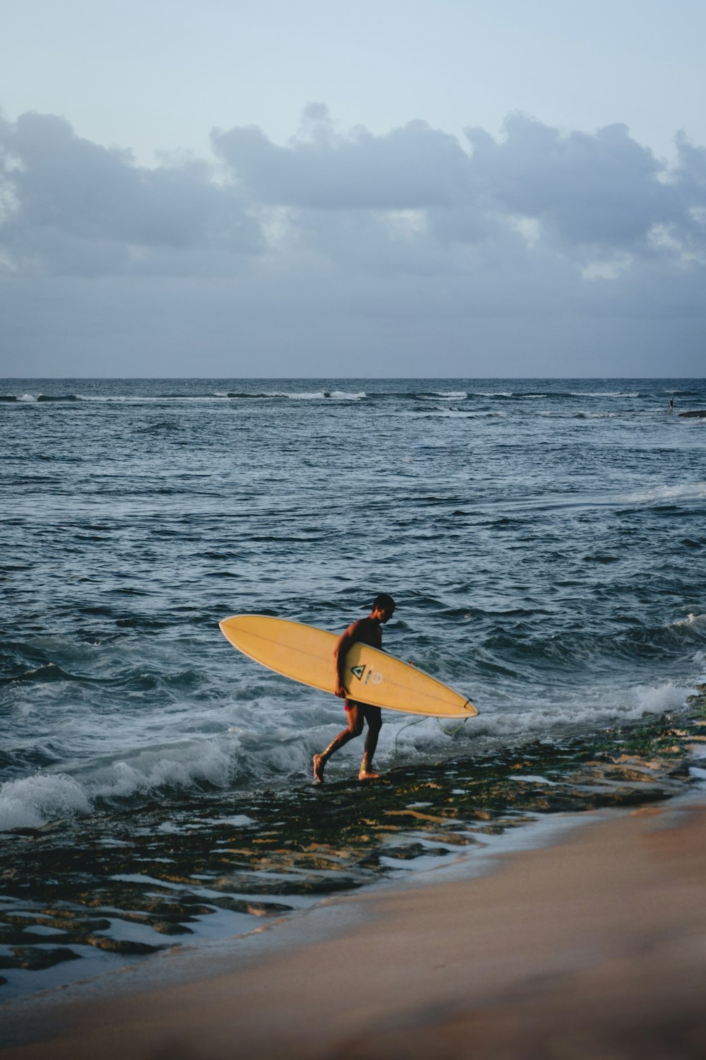 a man holding a yellow surfboard walking into the ocean