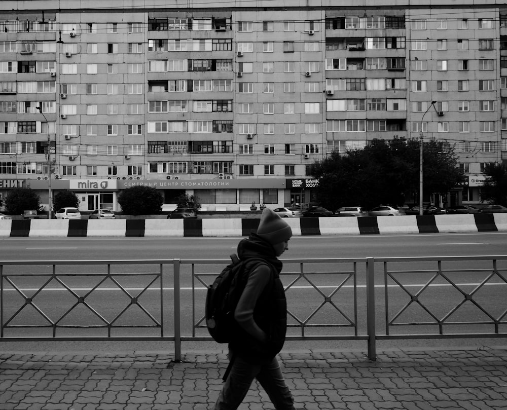 a man walking down a sidewalk in front of a tall building