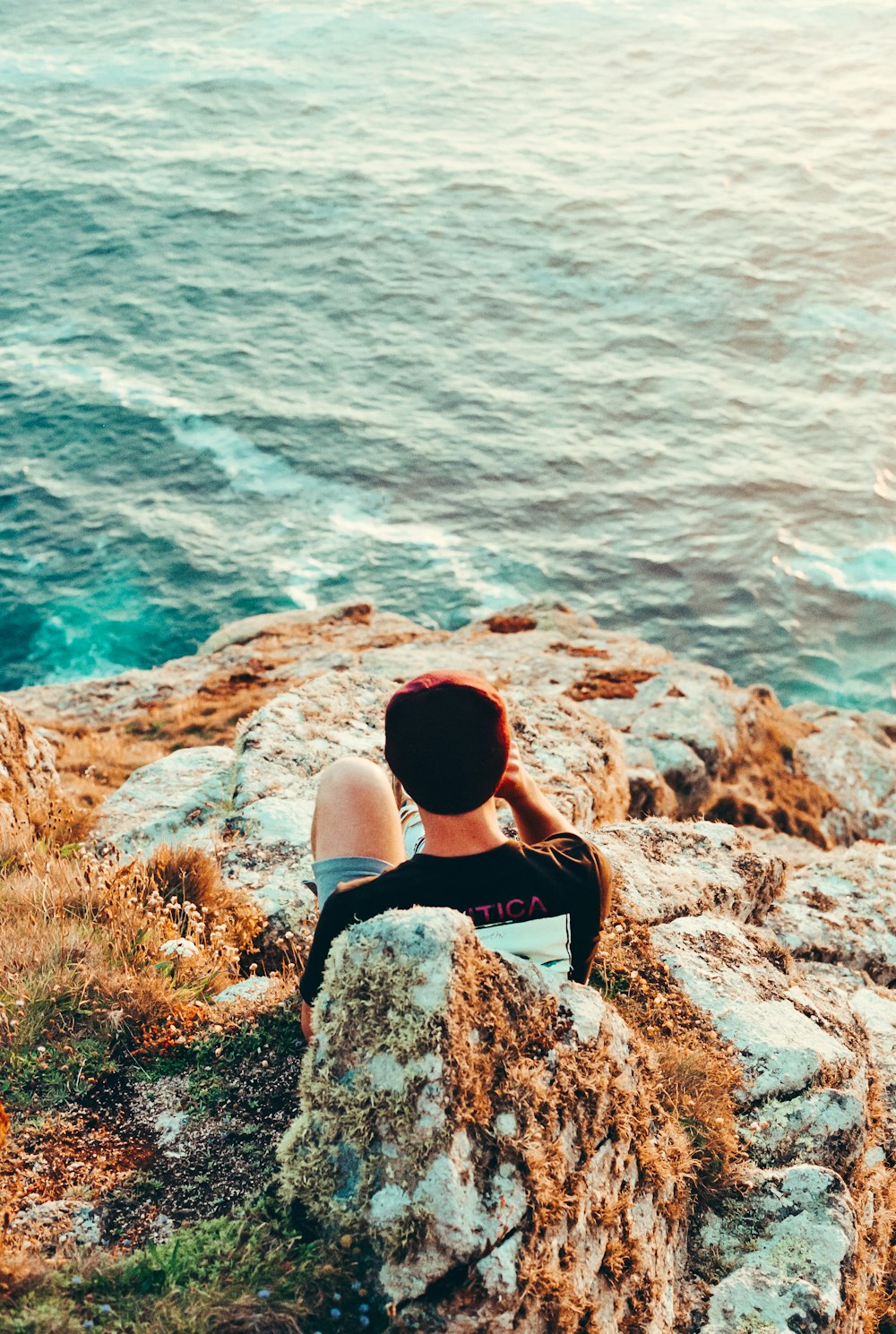 a person sitting on top of a rock next to the ocean