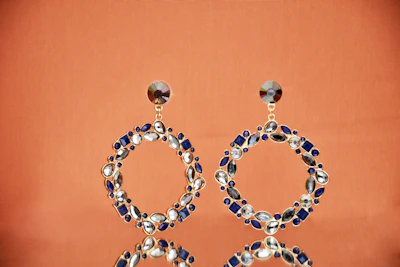 Elegant pair of gold hoop earrings adorned with tiny gemstones against a soft cream background.