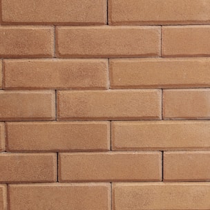 Close-up of a craftsman carefully laying bricks on a warm beige wall.