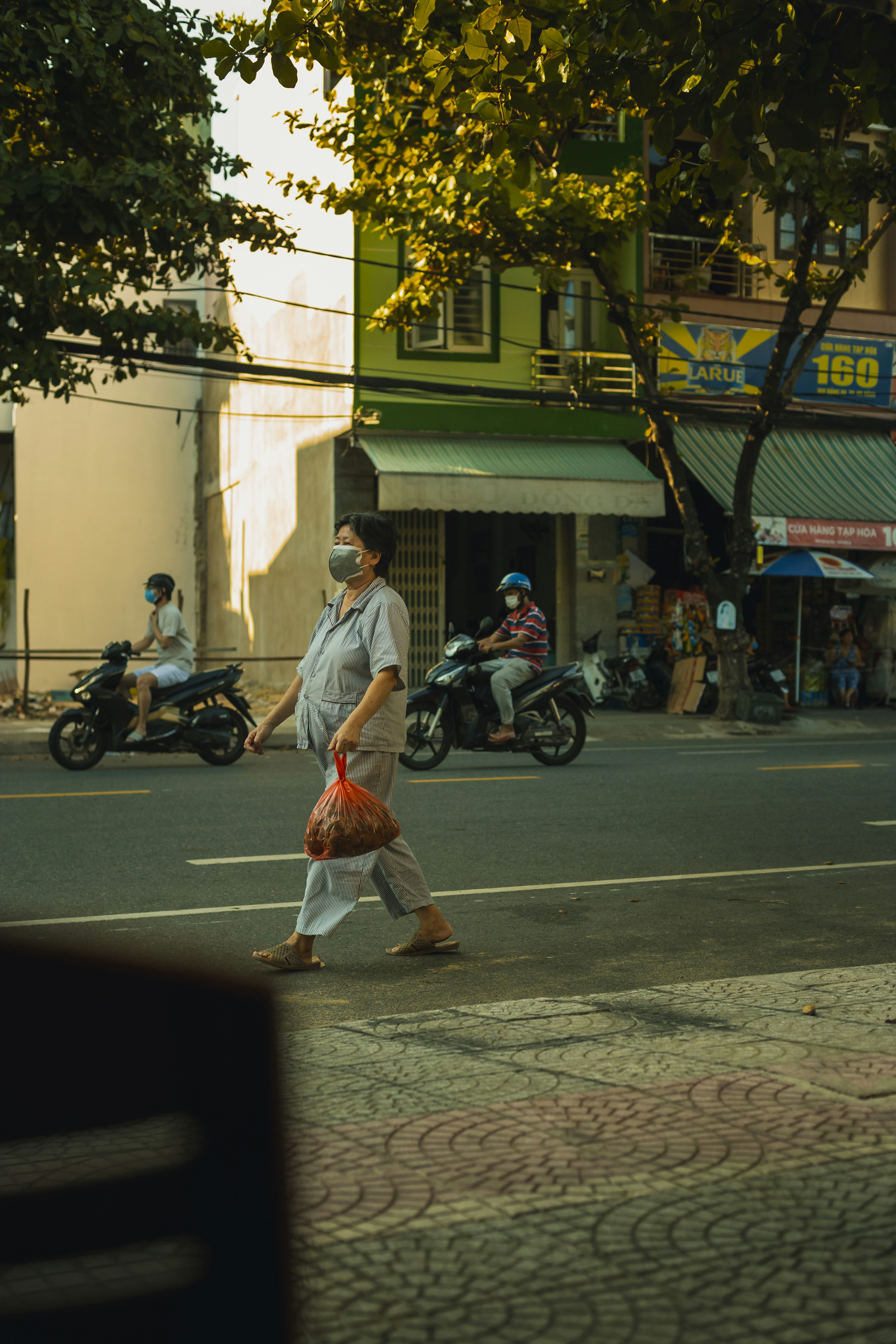Street scene with person walking and others on motorbikes, all wearing masks