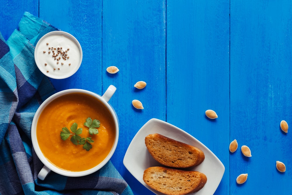 un tazón de sopa y dos trozos de pan en una mesa azul