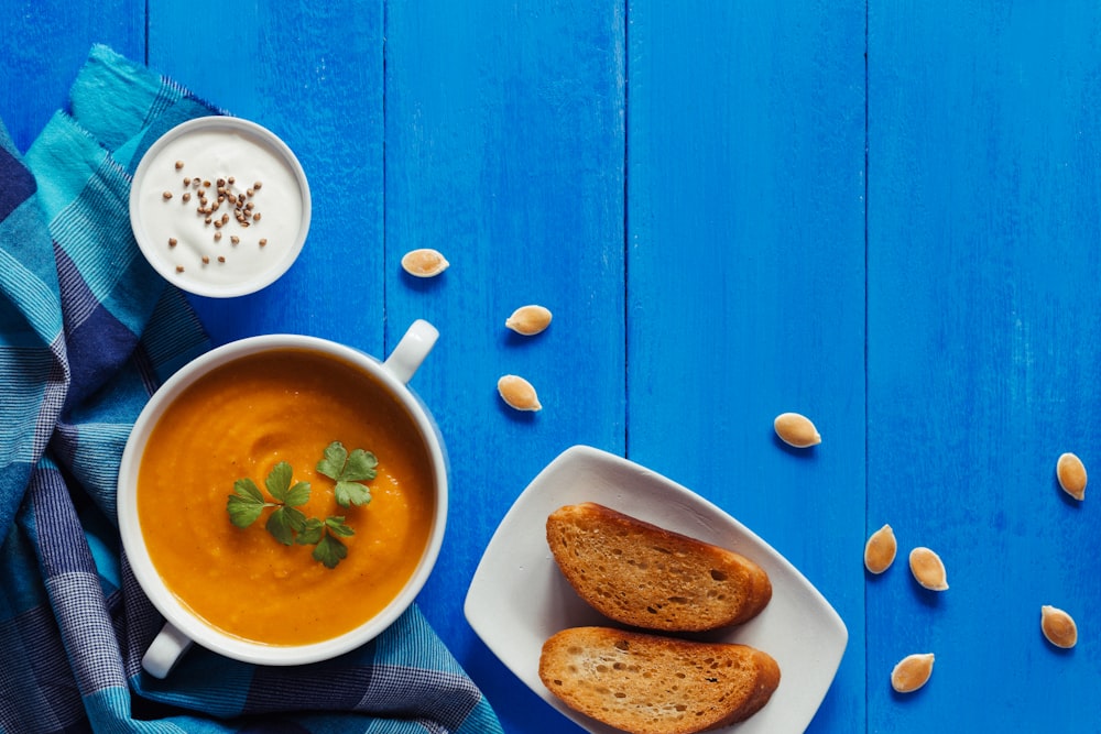a bowl of soup and two pieces of bread on a blue table