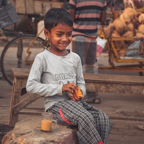 a young boy sitting on a bench with a glass of orange juice