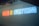 Neon lights display the phrase 'MEDIA IS EVERYTHING' in a sequence of red, yellow, and blue colors against a plain wall. The glow of the neon creates a vibrant and striking visual, infusing the scene with a modern and edgy look.