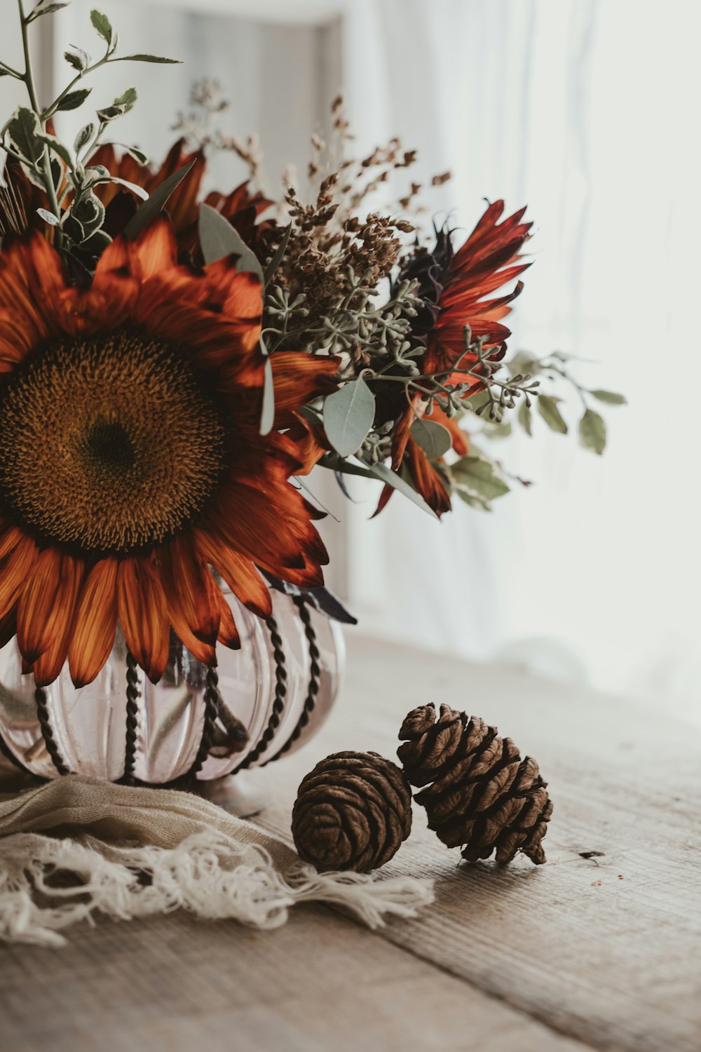 a vase with a sunflower and pine cones on a table