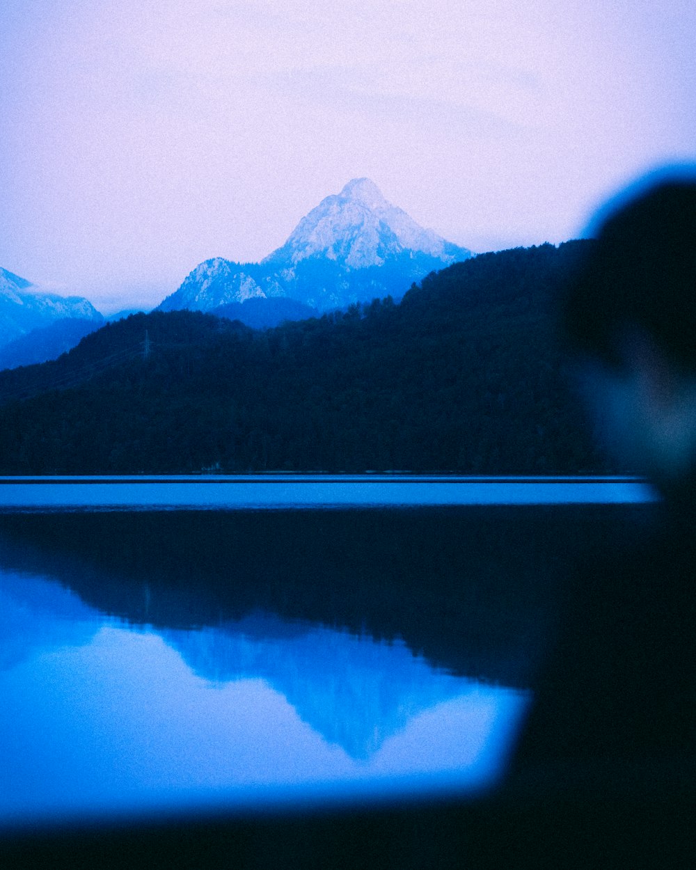 uma pessoa em pé na frente de um lago com uma montanha ao fundo