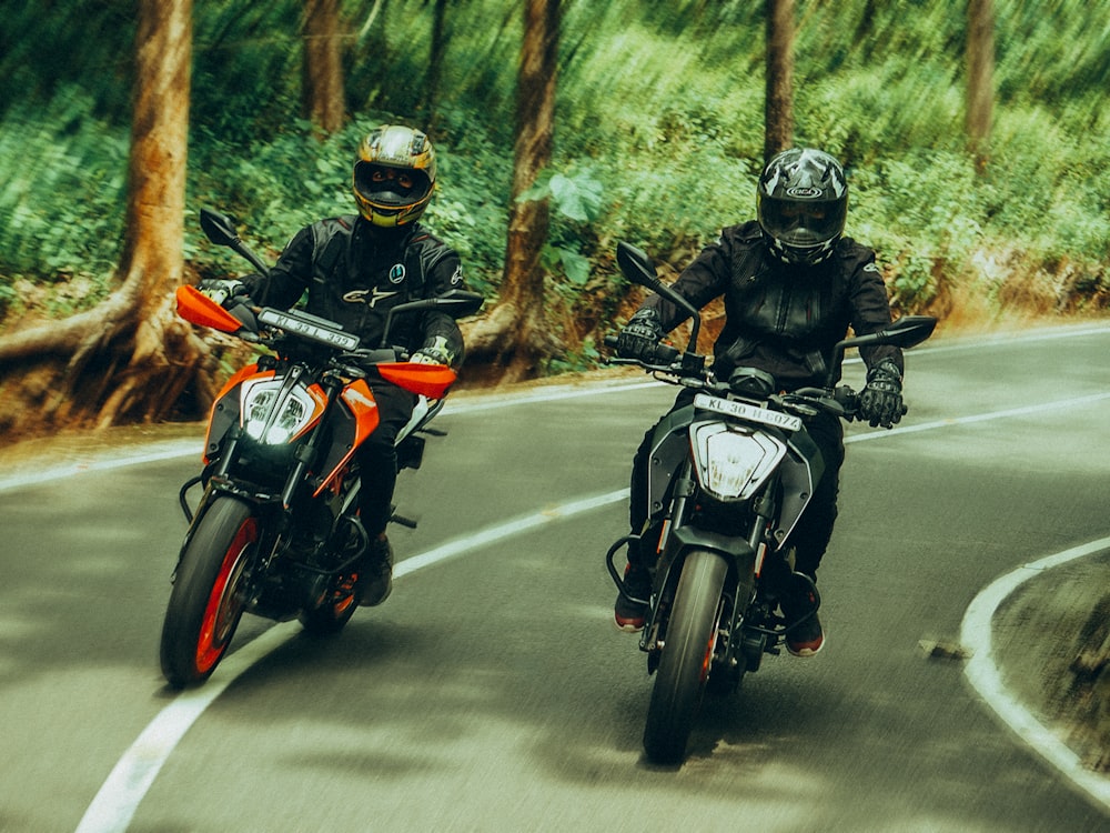 two people riding motorcycles on a road in the woods