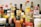 An assortment of various condiment bottles is arranged closely together. Brands such as Maggi and others with colorful labels and different shapes and sizes are visible. The image features a variety of bottles with red, yellow, and white caps.