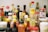 An assortment of various condiment bottles is arranged closely together. Brands such as Maggi and others with colorful labels and different shapes and sizes are visible. The image features a variety of bottles with red, yellow, and white caps.