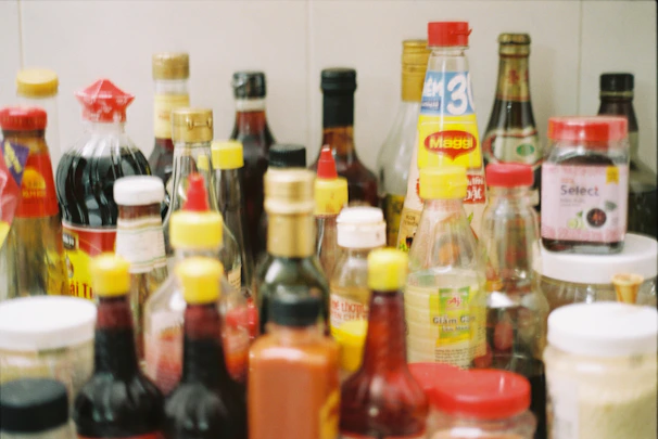 An overhead shot of assorted sauce bottles arranged neatly with fresh herbs and spices scattered around